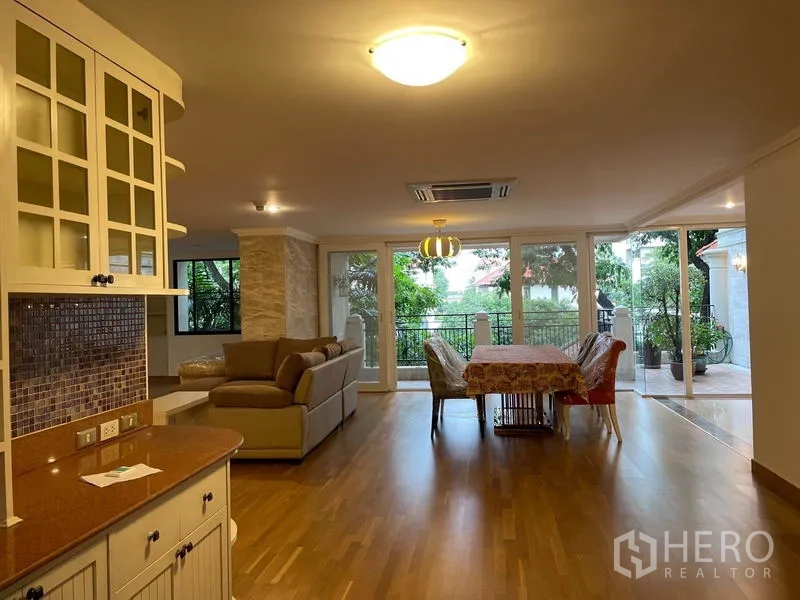 Condominium for rent in Watthana, Bangkok - Open-plan living and dining room leading to a balcony with lush garden views.