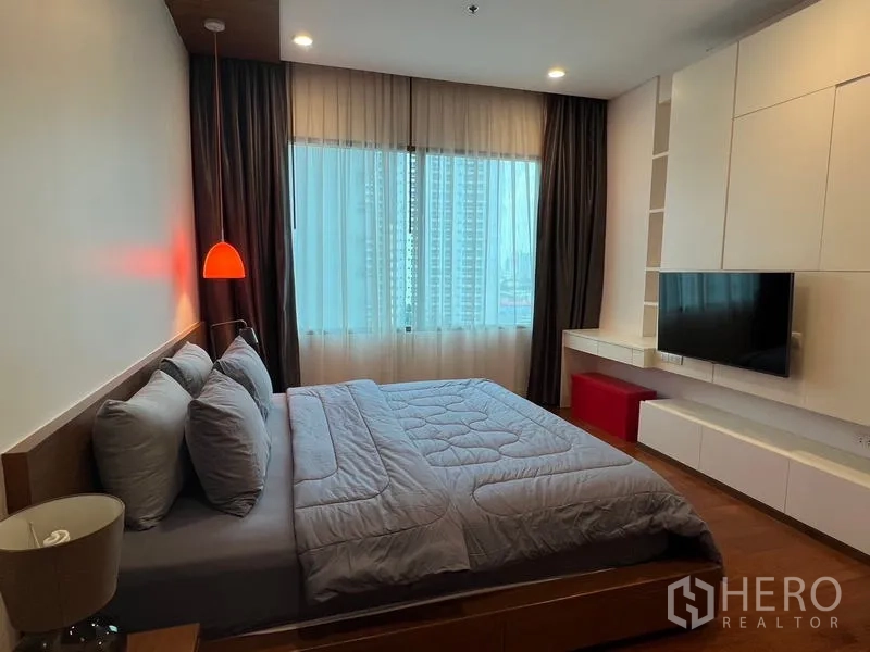 Condominium for rent in Khlong Toei, Bangkok - Bedroom showing wall-mounted TV, shelving and window with city outlook.