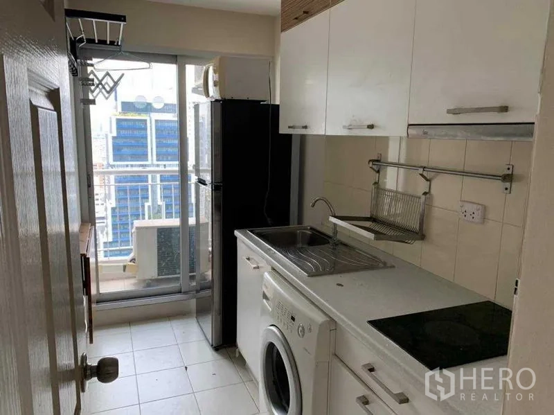 Condominium for rent in Bang Rak, Bangkok - Galley kitchen with white cabinets, sink, washing machine and balcony access.