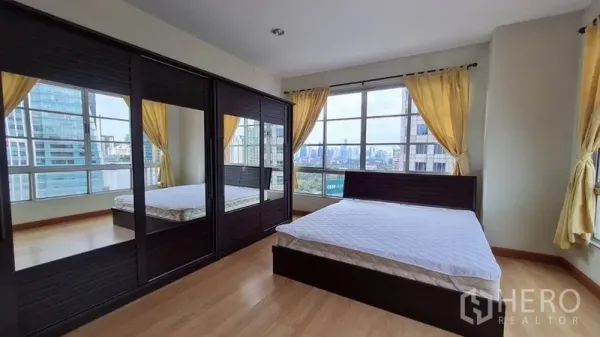 公寓 出租在Khlong Toei, Bangkok - 主卧配镜面衣柜、木地板与宽幅窗户城市景观。