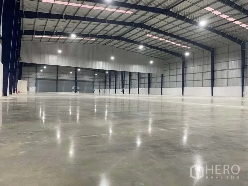 Warehouse for rent in Nonthaburi - Spacious clear‑span warehouse interior with polished concrete floor, high steel roof, and bright lighting.