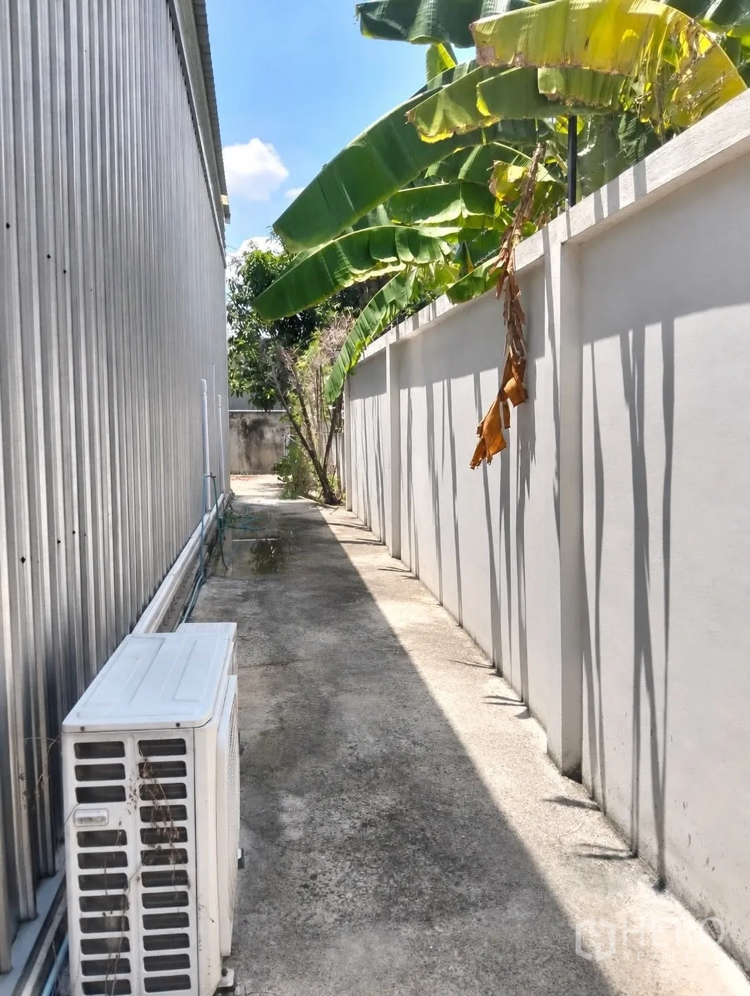 仓库 for rent in Don Mueang, Bangkok - 仓库侧边步道，旁有围墙、植被与室外空调机组。