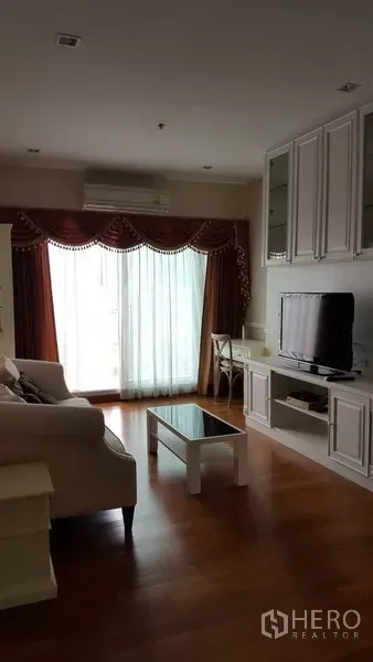 Condominium for rent in Bang Rak, Bangkok - Cozy living room with sofa, TV console, built-in cabinets and balcony door with curtains.