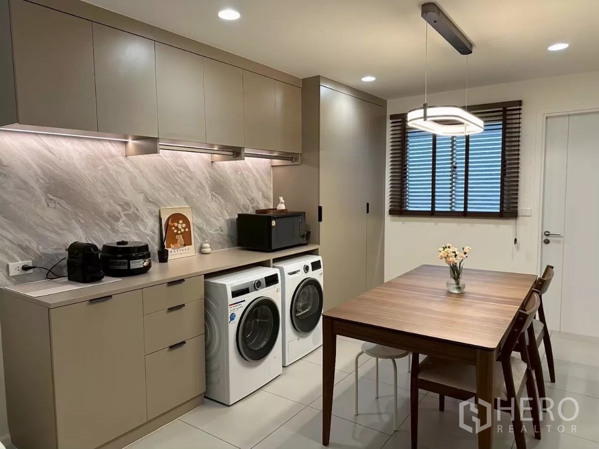 Townhouse for rent in Saphan Sung, Bangkok - Built-in pantry with marble-look backsplash, upper cabinets, and side-by-side washer and dryer next to the dining table.