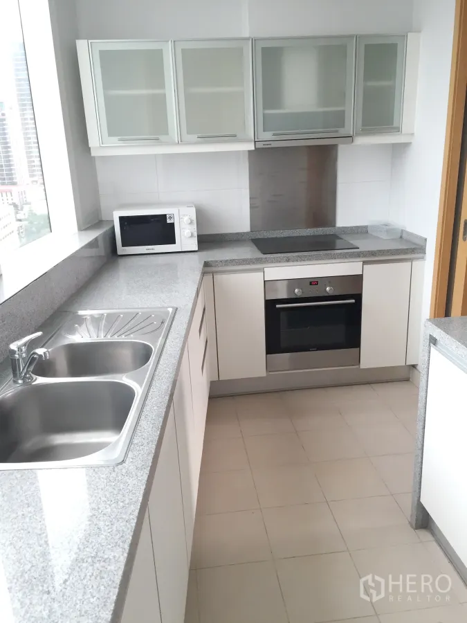 Condominium for rent in Khlong Toei, Bangkok - Bright separate kitchen with granite countertops, double sink, built-in oven and a city-view window.