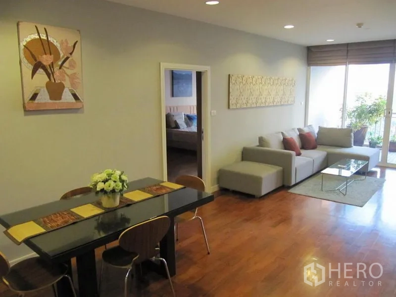 Condominium for rent in Khlong Toei, Bangkok - Dining corner with four-seat table facing the living area and balcony, accented by wall art and wood flooring.