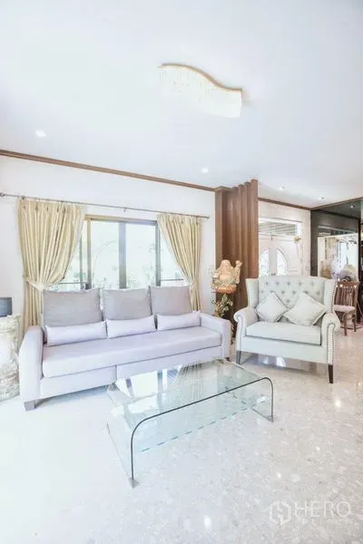 Detached House for sale in Lat Krabang, Bangkok - Bright living room with large window, light sofa, armchair and glass coffee table on polished floors.