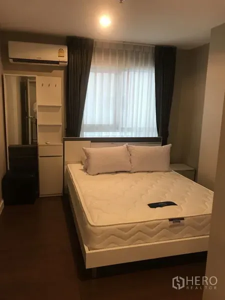 Condominium for rent or sale in Huai Khwang, Bangkok - Master bedroom with queen bed, air conditioner, wardrobe and soft lighting by a large window.