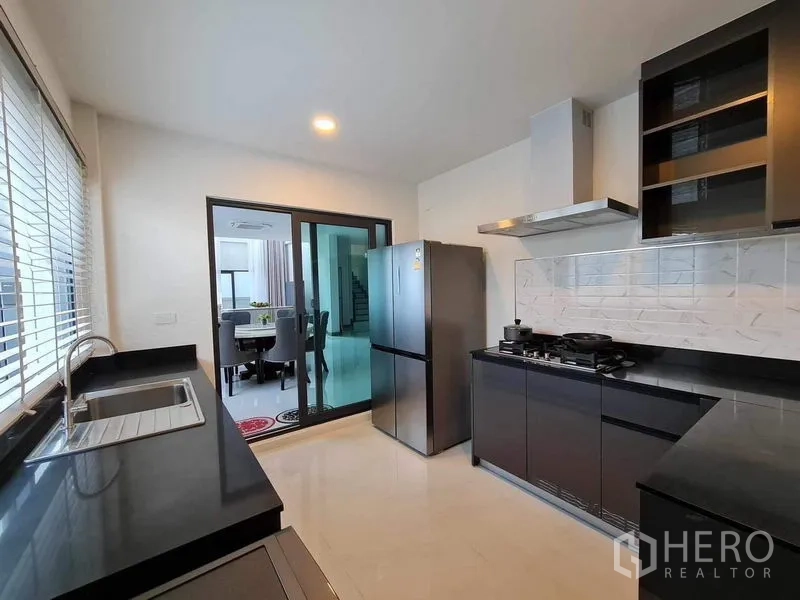 Detached House for rent or sale in Bang Phli, Samut Prakan - Western-style kitchen with black counters, gas stove and sliding door to dining.