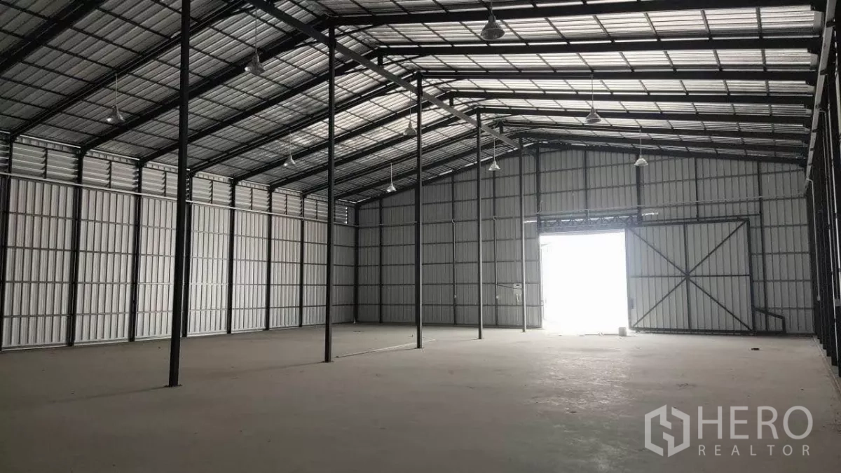 货栈 出租在Bang Lamung, Chon Buri - 仓库内部高挑空间，钢结构屋架、吊灯与混凝土地面。