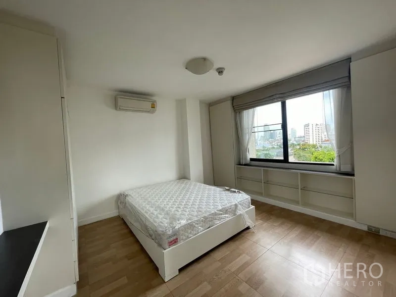 Condominium for rent in Watthana, Bangkok - Master bedroom with large window, built-in shelving and green outlook.