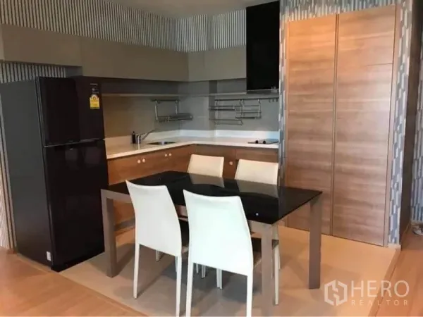 Condominium for rent or sale in Phaya Thai, Bangkok - Modern L-shaped kitchen with black fridge, ample cabinets and a glass-top dining table for four.