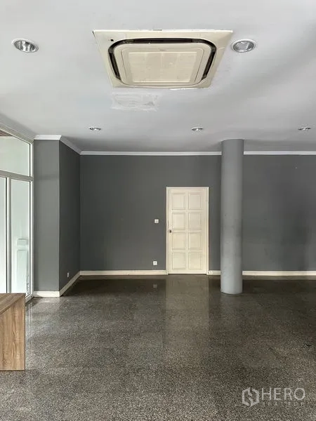 Townhouse for rent in Bang Kapi, Bangkok - Spacious open-plan room with dark grey walls, granite floors, a central column and cassette ceiling air-con.