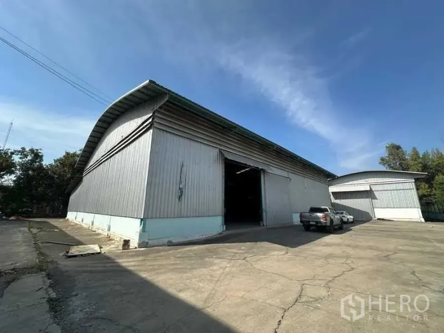 Warehouse for rent in Phra Nakhon Si Ayutthaya - Metal-clad warehouse exterior with high arched roof and wide driveway under blue sky.