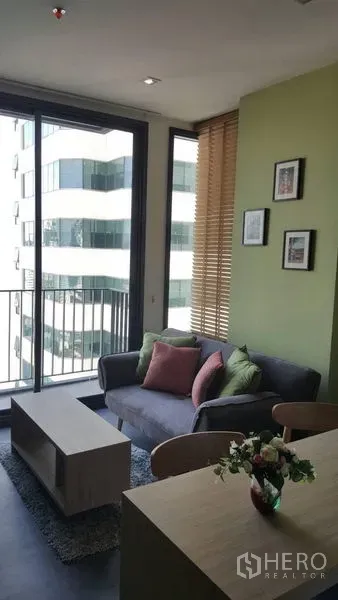 คอนโด ให้เช่าในWatthana, Bangkok - ห้องนั่งเล่นสว่าง มีโซฟา โต๊ะกลาง ระเบียงวิวเมือง ผนังสีเขียวและมู่ลี่ไม้