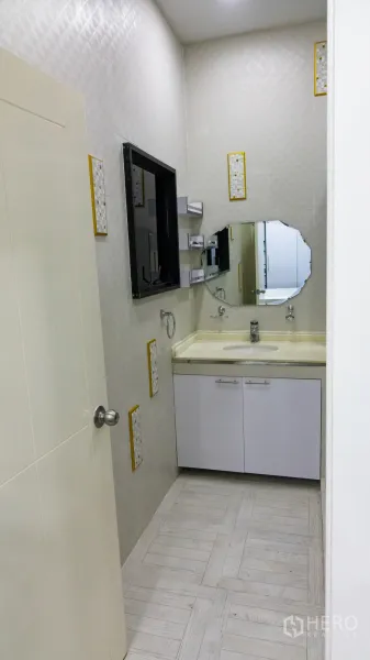 Condominium for rent or sale in Khlong Toei, Bangkok - Vanity area with cream countertop, storage cabinets and an octagonal mirror.