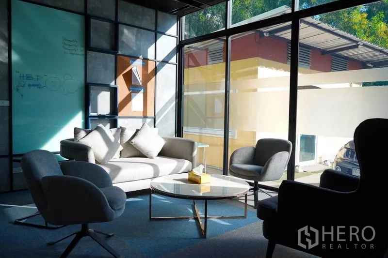 Office Space for rent in Bang Na, Bangkok - Sunlit lounge with grey sofa, armchairs and round coffee table by floor‑to‑ceiling windows.