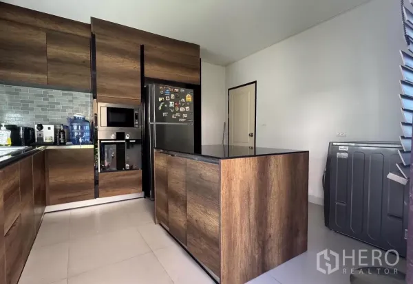 Detached House for sale in Lat Krabang, Bangkok - Modern U-shaped kitchen with wood cabinetry, island, built-in microwave and subway tile backsplash.