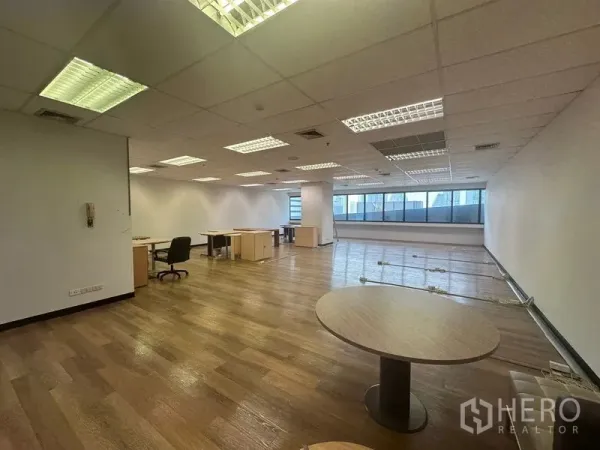 Office Space for rent in Bang Rak, Bangkok - Spacious workspace with desks, a round meeting table, large windows and overhead fluorescent lighting.