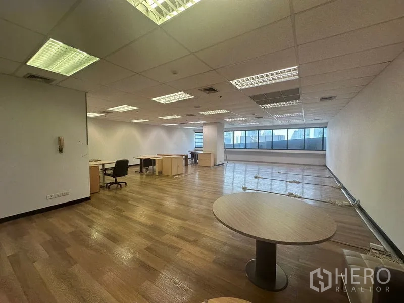 Office Space for rent in Bang Rak, Bangkok - Spacious workspace with desks, a round meeting table, large windows and overhead fluorescent lighting.