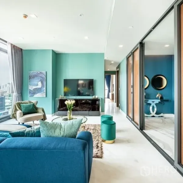 Condominium for rent or sale in Watthana, Bangkok - Bright living room with teal walls, TV console, large windows and sliding glass doors to the bedrooms.