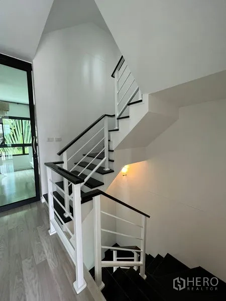 Townhouse for sale in Bang Kapi, Bangkok - Staircase landing with white railings and a warm wall sconce.