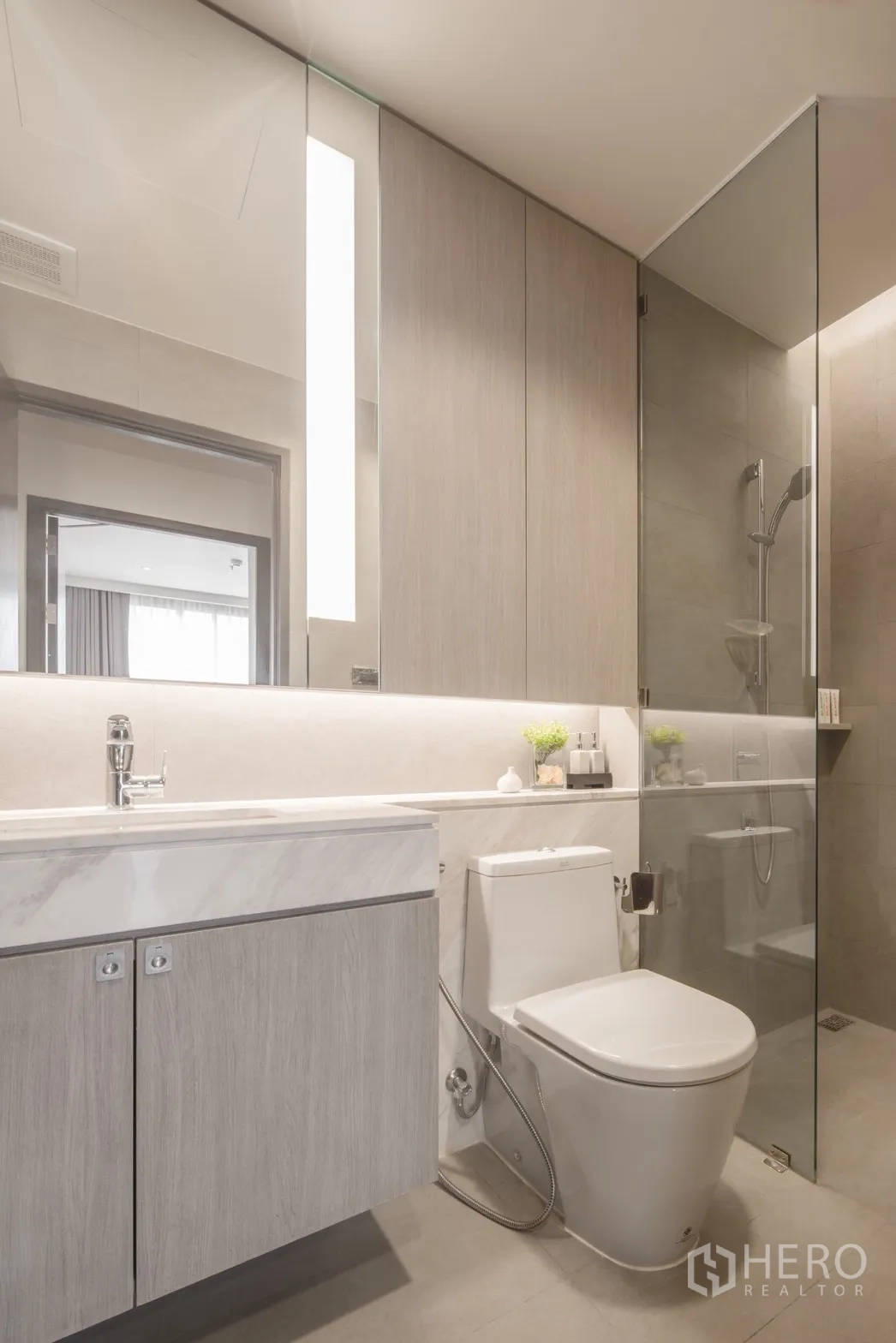 Condominium for rent in Khlong Toei, Bangkok - Modern bathroom with large mirror, vanity storage and toilet.
