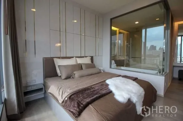 公寓 出售在Watthana, Bangkok - 主卧配软包床与落地窗，玻璃墙可望套内浴室的浴缸及城市天际线。