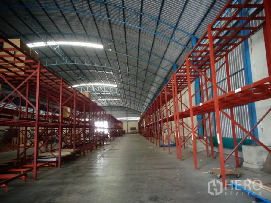 货栈 出租或出售在Lat Lum Kaeo, Pathum Thani - 长走道两侧布满红色货架，蓝色桁架屋顶延伸。