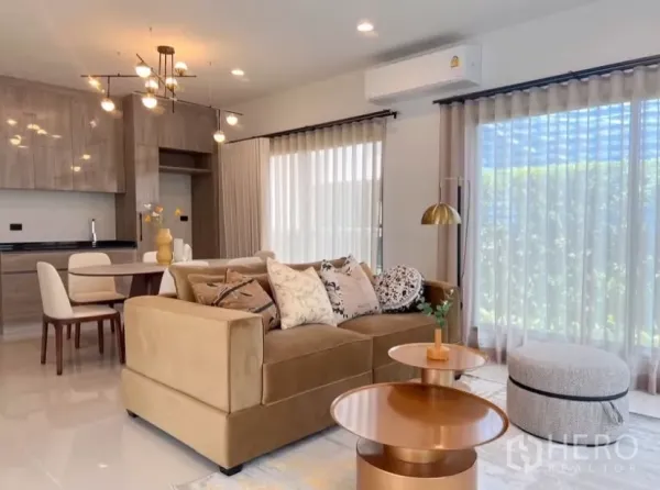 บ้าน ให้เช่าหรือขายในBang Kapi, Bangkok - ห้องนั่งเล่นสว่างโปร่ง โซฟาสีเบจ โต๊ะกลางสีทอง ม่านสูงจรดเพดานติดกับครัวบิวต์อิน