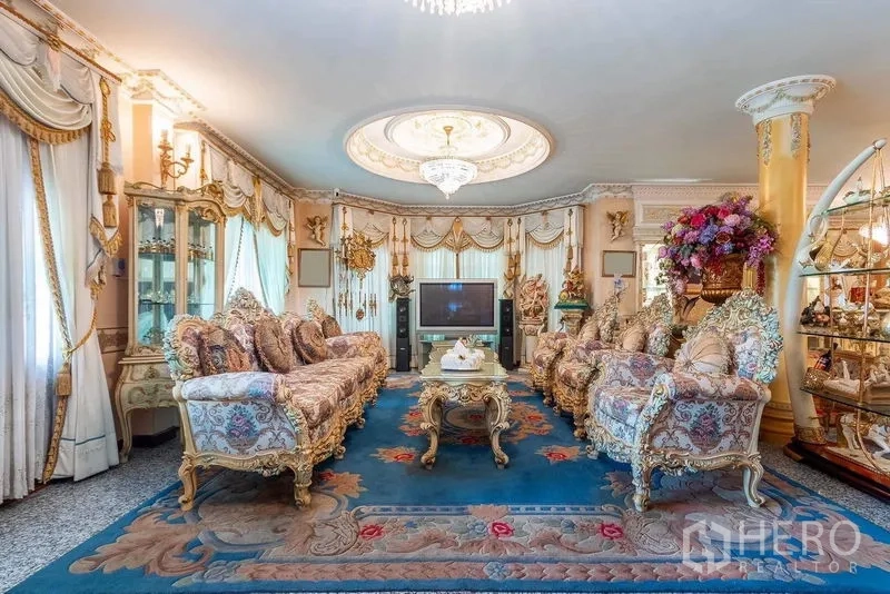 Detached House for rent or sale in Bang Khen, Bangkok - Elegant living room featuring ornate sofas, chandelier ceiling, decorative curtains, and a large area rug.