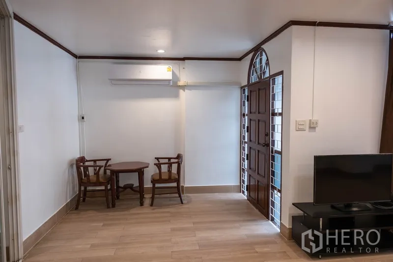 Home Office for rent in Khlong Toei, Bangkok - Entry lounge with small table set, TV stand and arched wooden door.