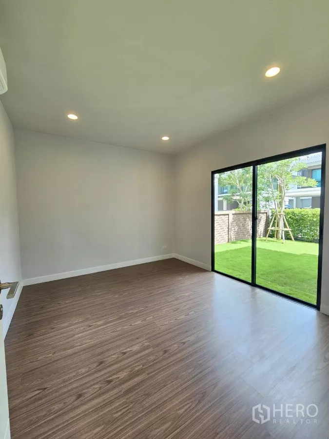 Detached House for sale in Lam Luk Ka, Pathum Thani - Ground-floor bedroom with wood-style flooring and sliding glass doors to the garden.