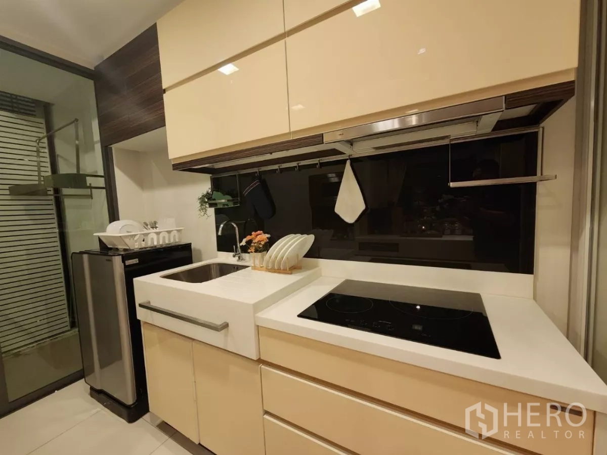 Condominium for rent in Phra Khanong, Bangkok - Kitchen with sink, induction hob, fridge, and glass backsplash.