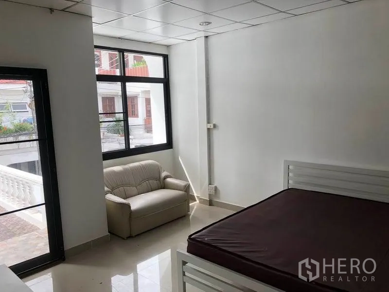 Townhouse for rent in Watthana, Bangkok - Bright bedroom with large windows, small sofa and access to a balcony.