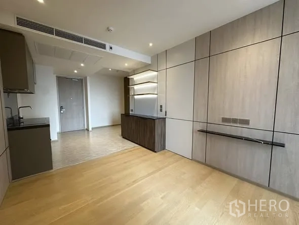 Condominium for sale in Din Daeng, Bangkok - Living area featuring wall paneling, floating TV shelf, and a kitchenette opposite the entrance.