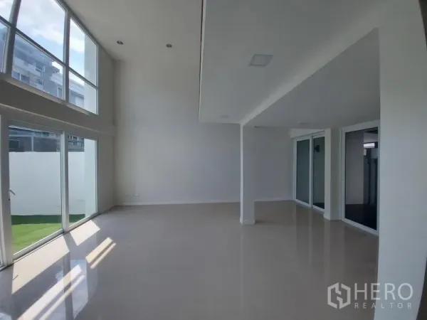 联排别墅 出售在Wang Thonglang, Bangkok - 通透明亮的开放式区域，双层挑高天花与转角落地窗，面向私家草坪。