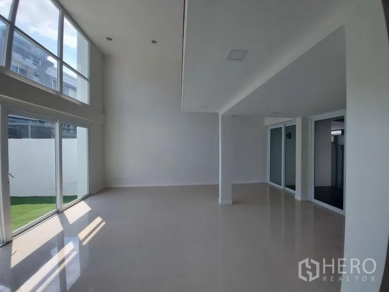 联排别墅 出售在Wang Thonglang, Bangkok - 通透明亮的开放式区域，双层挑高天花与转角落地窗，面向私家草坪。
