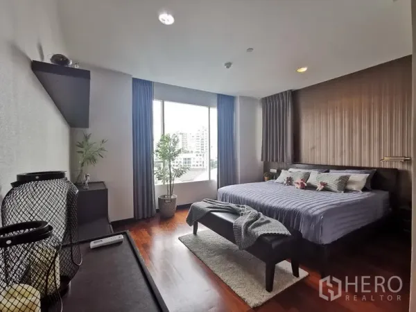 Condominium for rent or sale in Khlong Toei, Bangkok - Master bedroom with king bed, accent wall, wood floors, and a large window with city views.