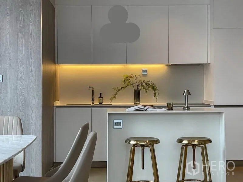 Condominium for rent in Watthana, Bangkok - Modern kitchen with white cabinetry, under-cabinet lighting, and a marble island with gold bar stools.
