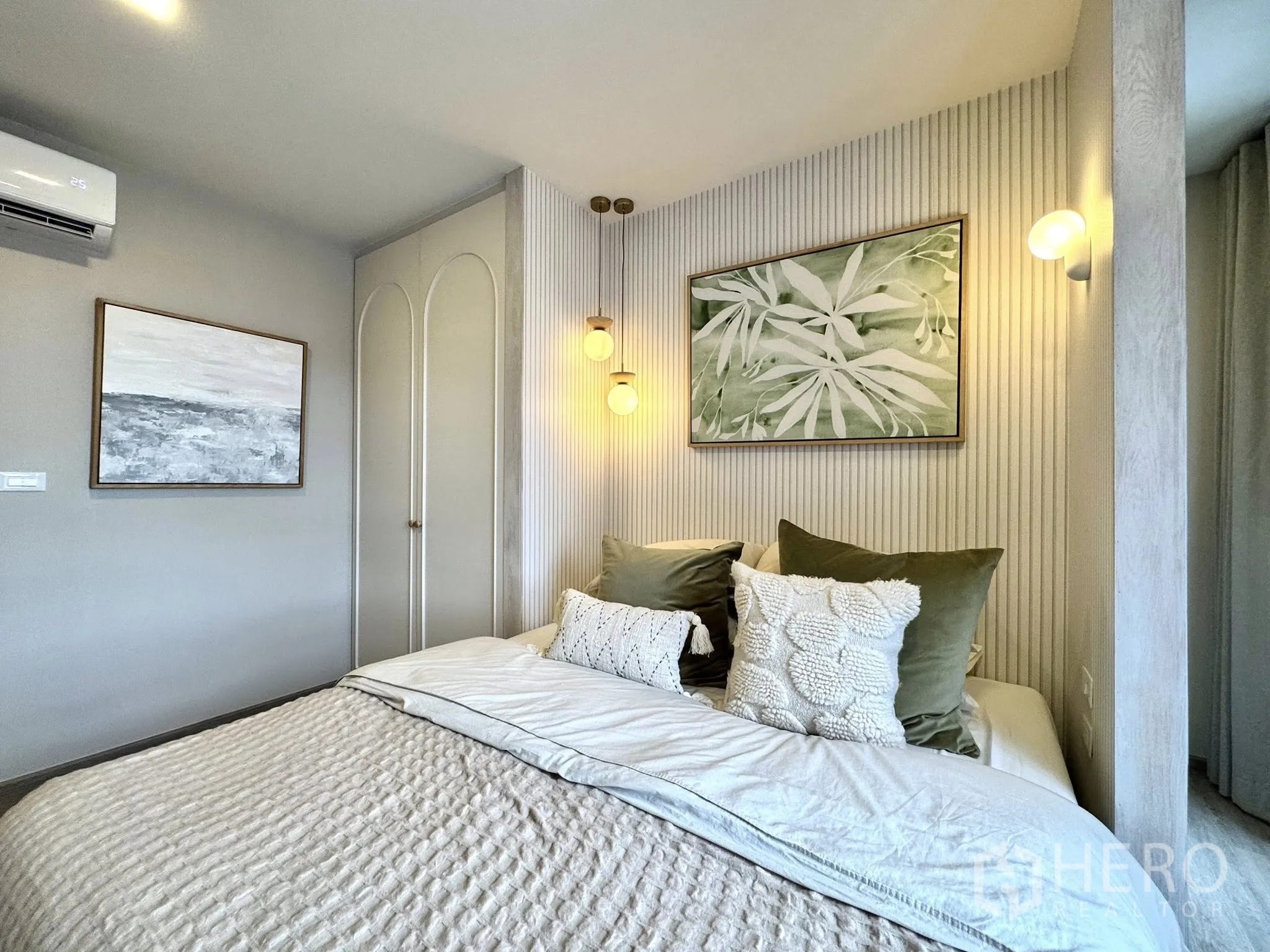 Condominium for rent in Watthana, Bangkok - Second bedroom angle showing soft bedding, wall sconces, artwork, and air conditioner.