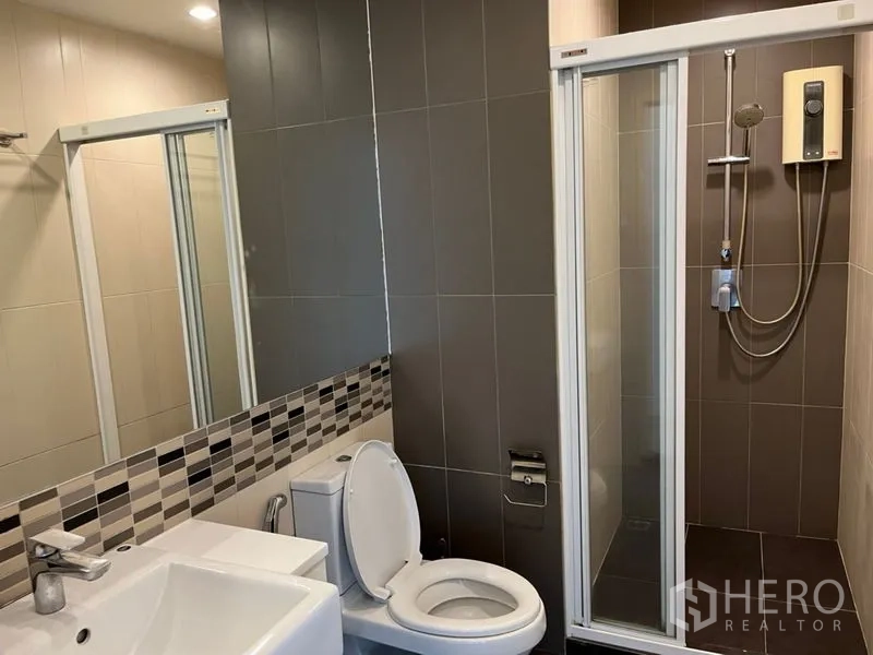 Condominium for sale in Phaya Thai, Bangkok - Bathroom with glass-enclosed shower, vanity and toilet in neutral tiles.