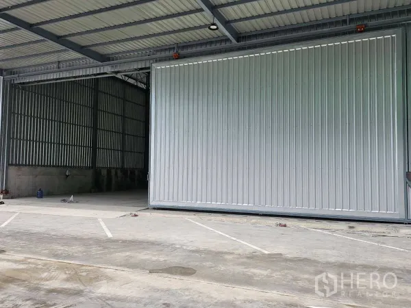 Warehouse for rent in Lam Luk Ka, Pathum Thani - Wide concrete yard with marked parking in front of an industrial sliding door.