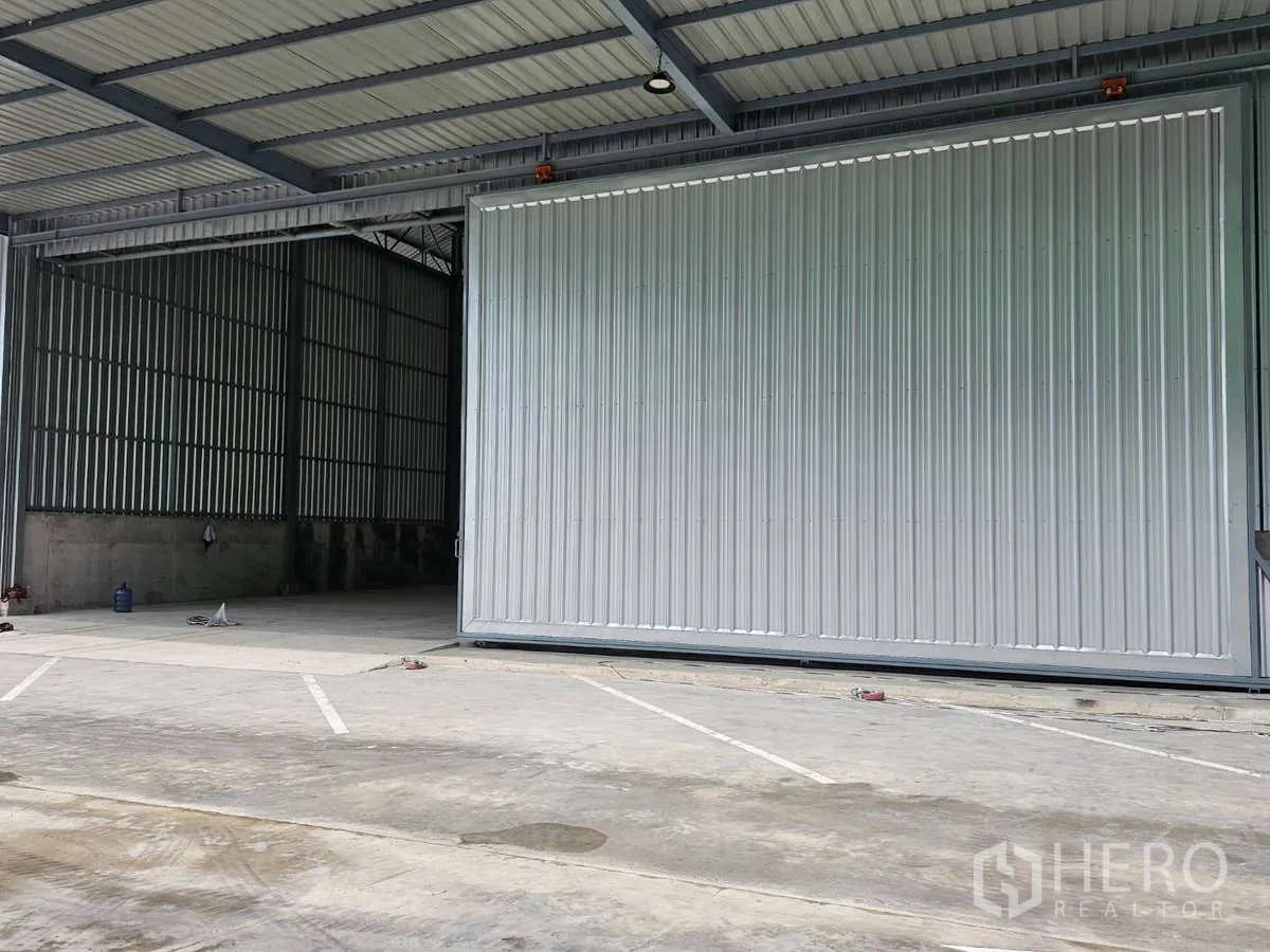 Warehouse for rent in Lam Luk Ka, Pathum Thani - Wide concrete yard with marked parking in front of an industrial sliding door.