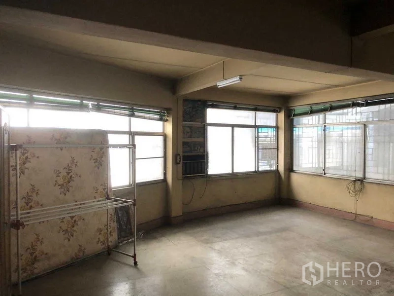 Shophouse for rent in Khlong Toei, Bangkok - Corner room with multiple windows and shelving, ready for refurbishment.
