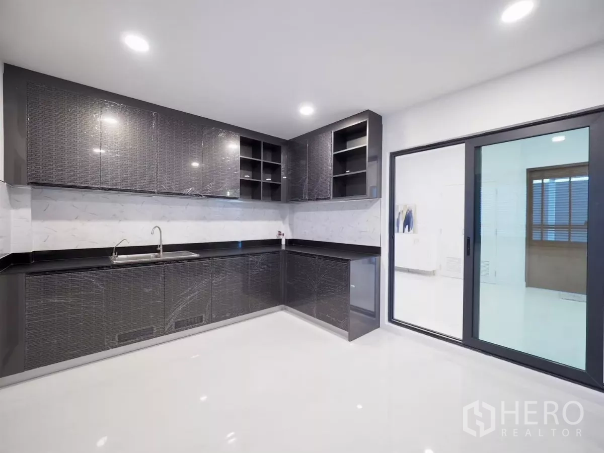 独立式住宅 出租在Bang Phli, Samut Prakan - 厨房转角，大量橱柜、双水槽及玻璃推拉门。