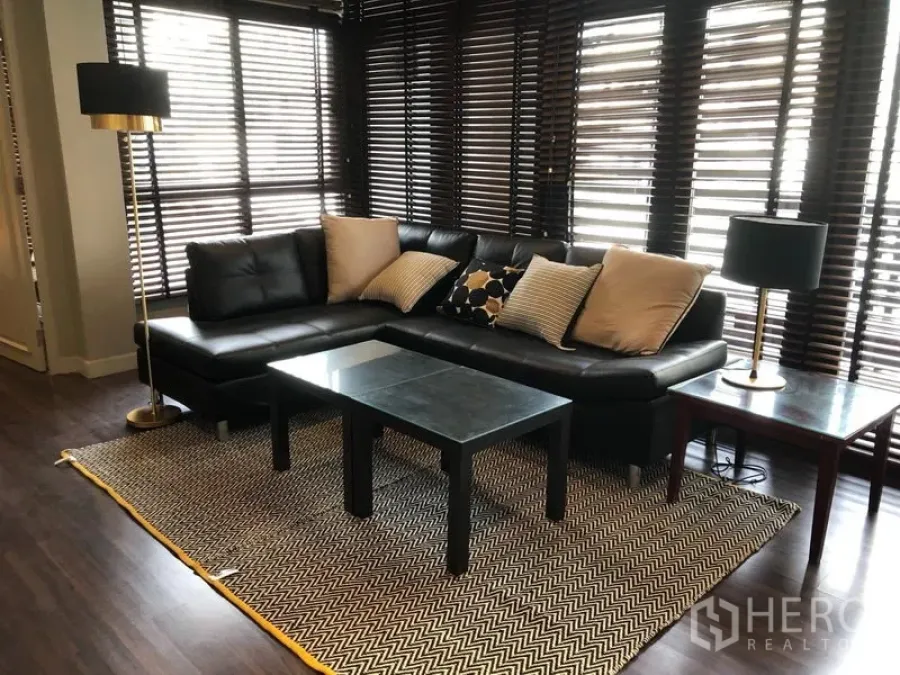 公寓 出租在Khlong Toei, Bangkok - 明亮客厅，黑色转角皮沙发、茶几与人字纹地毯，临落地窗。