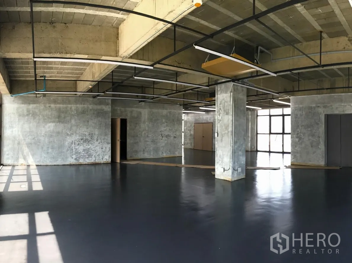 Office Space for rent in Khlong Toei, Bangkok - Corner section of shell office with exposed services, ceiling cable trays, concrete pillar, and multiple windows ideal for flexible layouts.