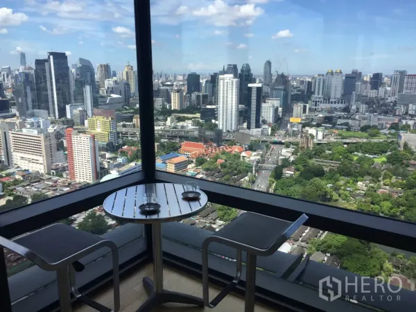 公寓 出租或出售在Ratchathewi, Bangkok - 转角阳台配高脚桌椅，环绕城市全景。