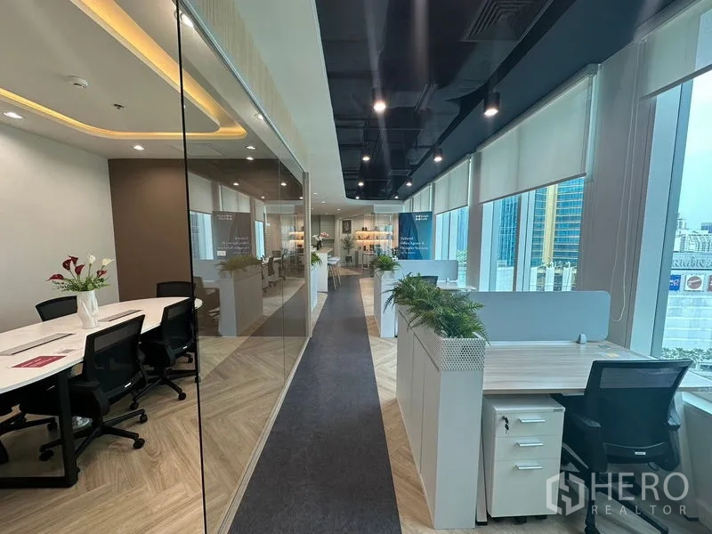 Office Space for rent - Corridor of workstations by large windows, glass meeting room and skyline outside.